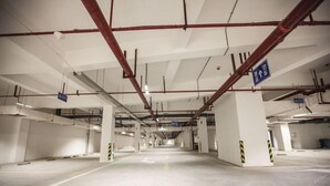 An empty parking garage with white pillars, yellow and black striped safety lines, and directional signs. - Vienna International Hotel (Changsha)