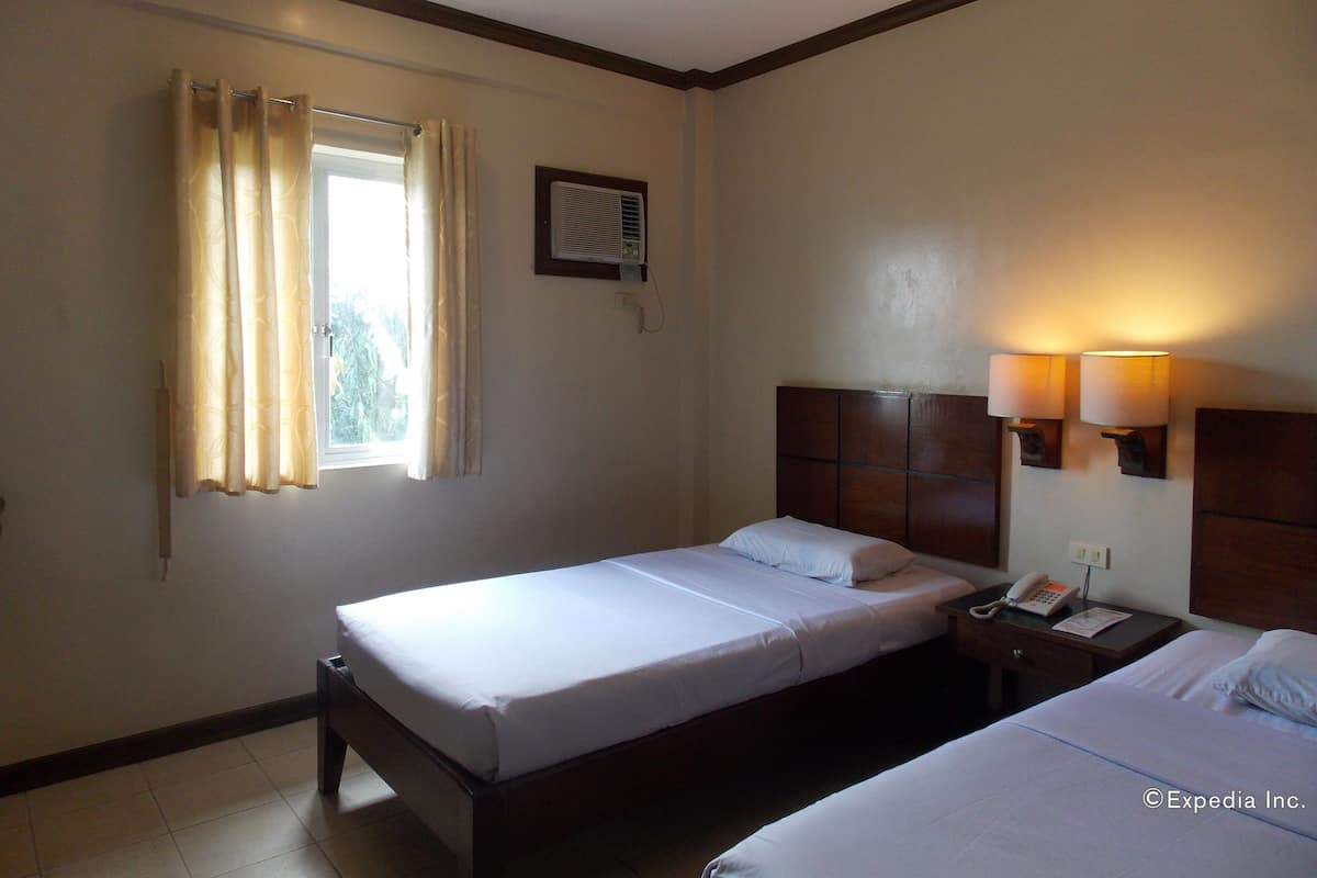 Una habitación de hotel con cama, una mesita de noche con teléfono y una ventana con cortinas.