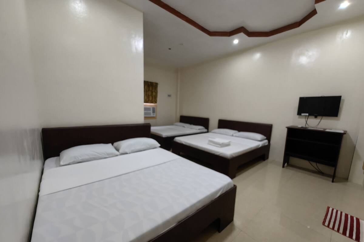 A hotel room with three beds, a flat-screen TV, and a small desk.