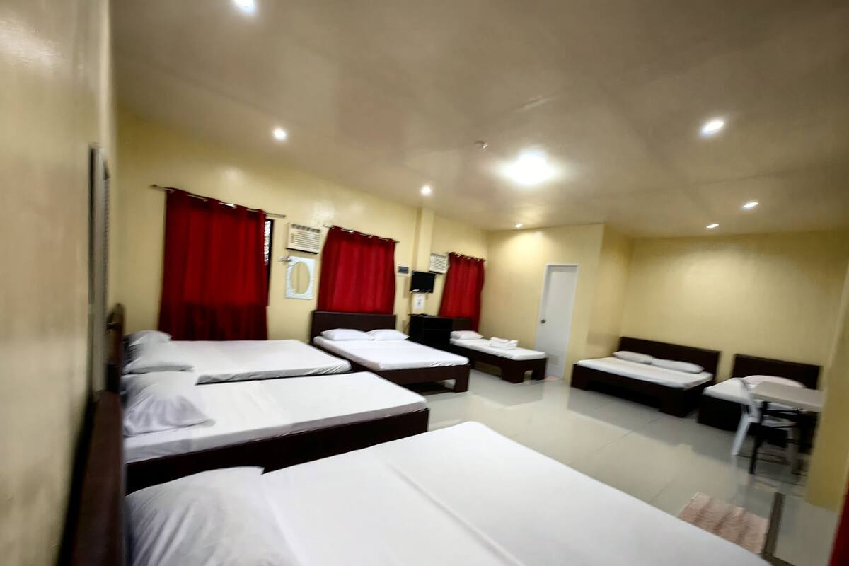 A hotel room with four single beds, a small desk, a chair, and a door.