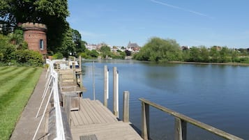 Un muelle de madera se adentra en aguas tranquilas, con un edificio de ladrillo y vegetación a un lado.