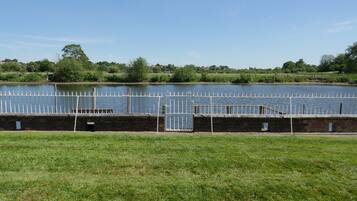 A grassy area with a white metal fence and a body of water.