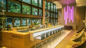 Eine moderne Bar mit einer langen Theke, mehreren Barhocker und einer Sitzecke mit gemusterten Kissen.