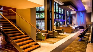 Eine moderne Hotelhalle mit Treppe, Sitzgelegenheiten, Bar und großen Fenstern.