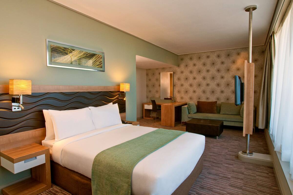 Une chambre d’hôtel avec un grand lit, un bureau, une chaise, un canapé et une télévision.