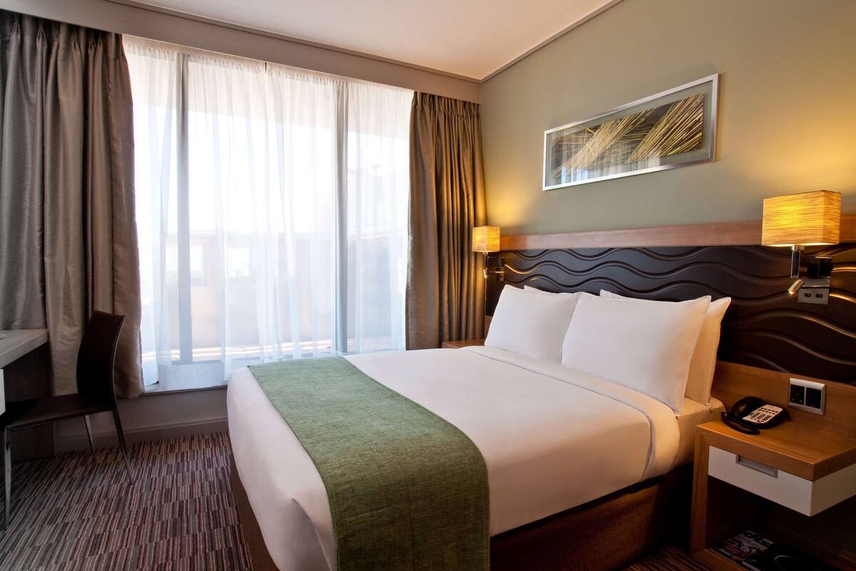 Une chambre d’hôtel avec un grand lit, un bureau, une chaise, une lampe et un tableau au mur.