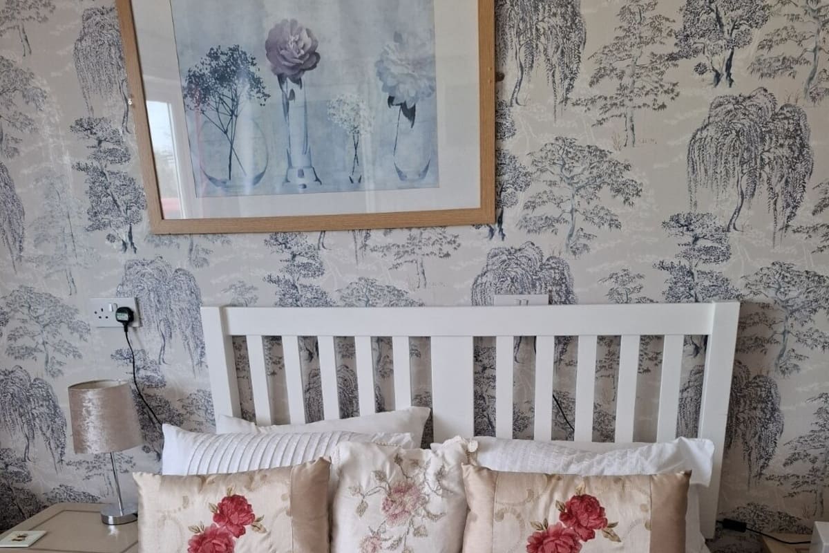 A bedroom with a white bed, floral pillows, a wooden headboard, and a framed artwork above the bed.