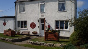 A white building with the number 1860 on the door, a bench, and flower planters.