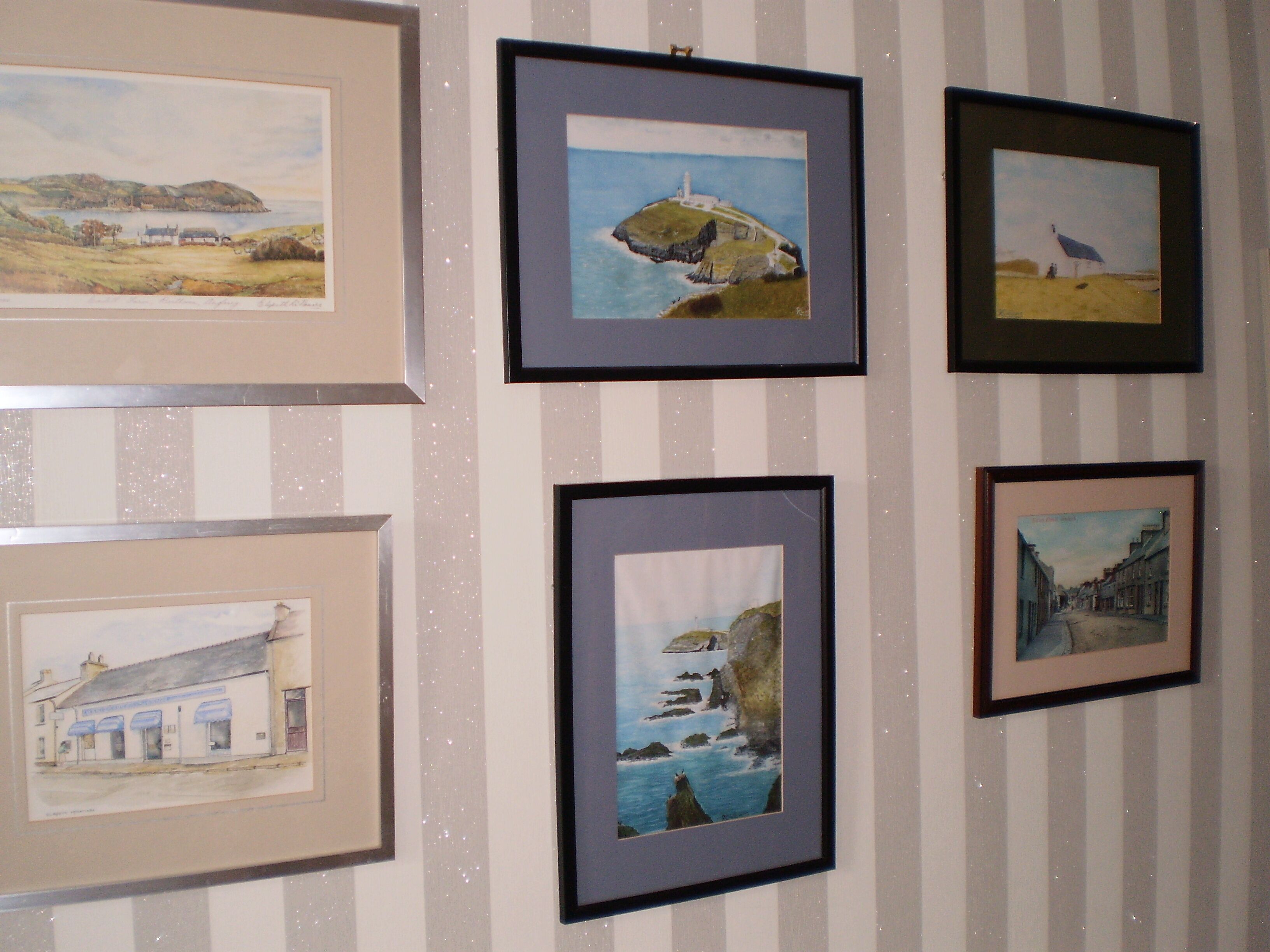 A wall with six framed artworks depicting coastal scenes.