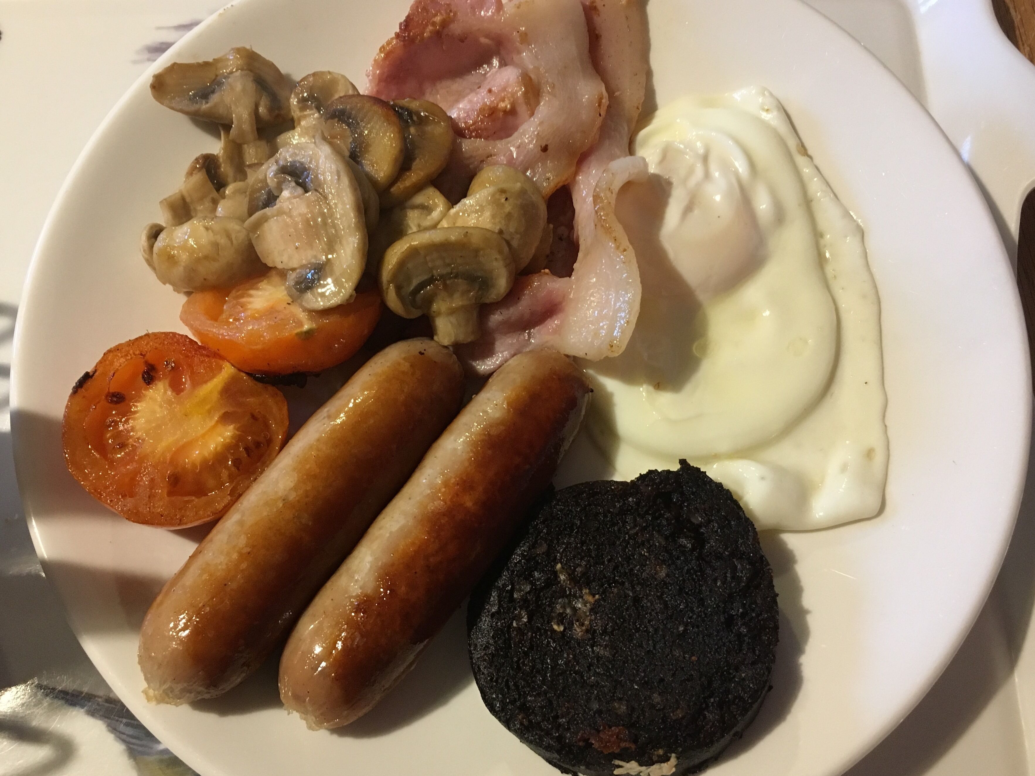 A plate with sausages, mushrooms, bacon, a slice of tomato, and a poached egg.