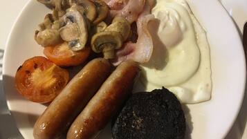 Ein Teller mit Würstchen, Pilzen, Speck, einer Tomatenscheibe und einem pochierten Ei.