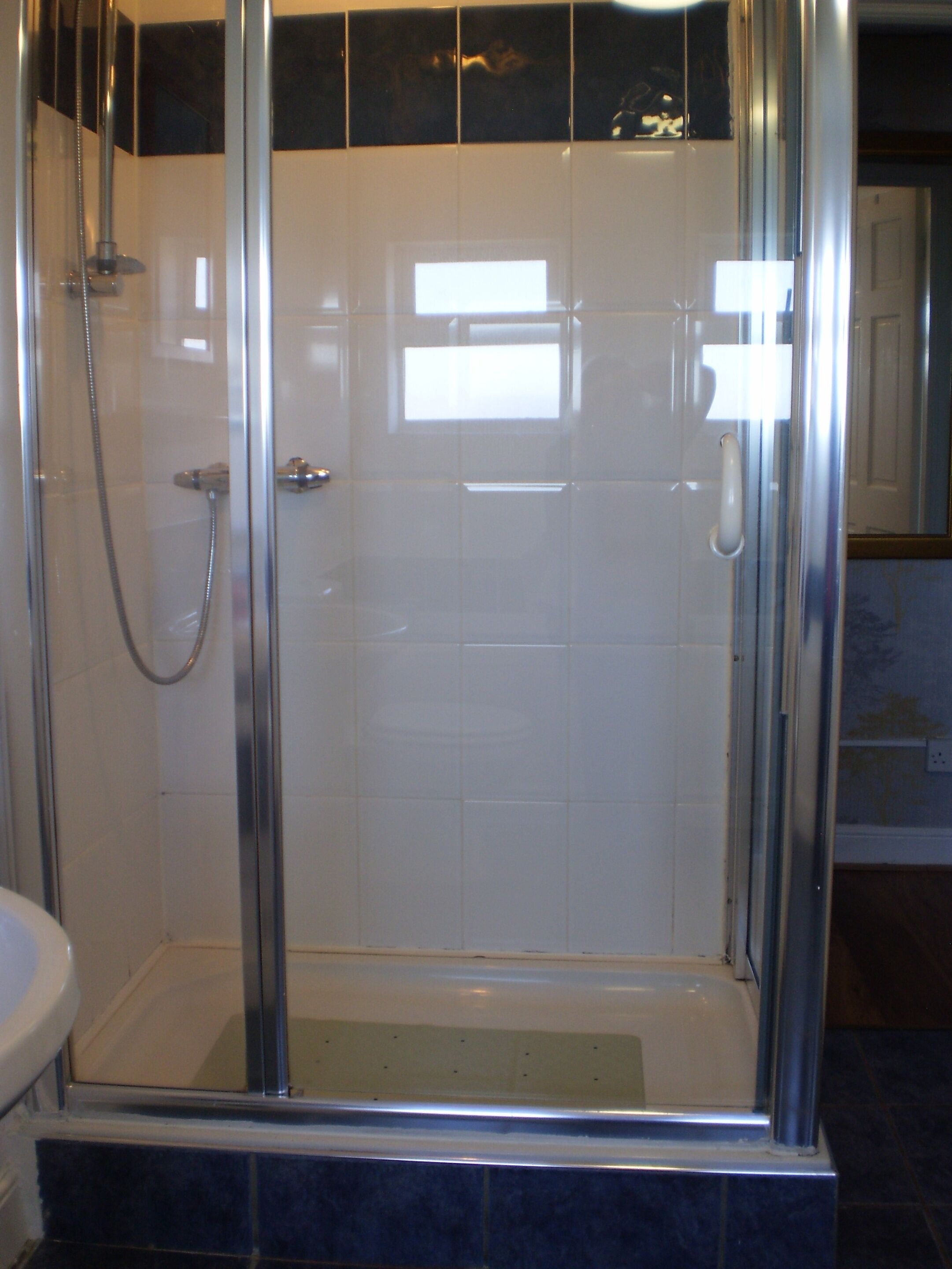 A glass-enclosed shower stall with a tiled wall and a visible door handle.