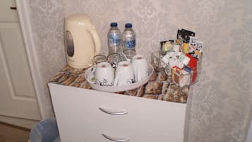 A kitchen counter with a coffee maker, water bottles, a bowl of mugs, and a basket of food items.