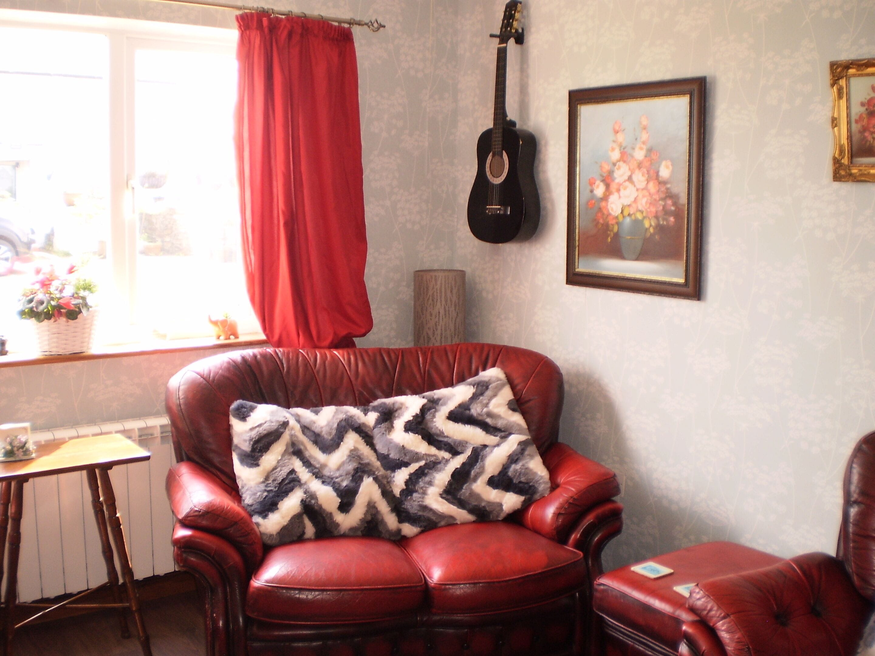 Une pièce avec un fauteuil en cuir rouge, une guitare noire et un tableau floral encadré accroché au mur.
