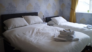 A hotel room with two beds, each with white linens and pillows. There is a window with yellow curtains, and a small plant on the windowsill.