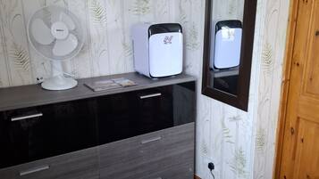Ein Schlafzimmer mit einem Holzschrank, einem Standventilator, einem Heizgerät und einem Spiegel an der Wand.