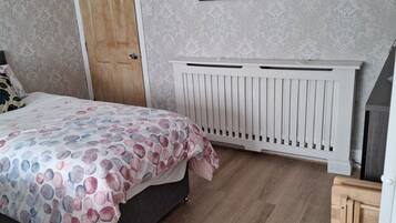 A bedroom with a bed, a radiator, a door, and a framed picture on the wall.