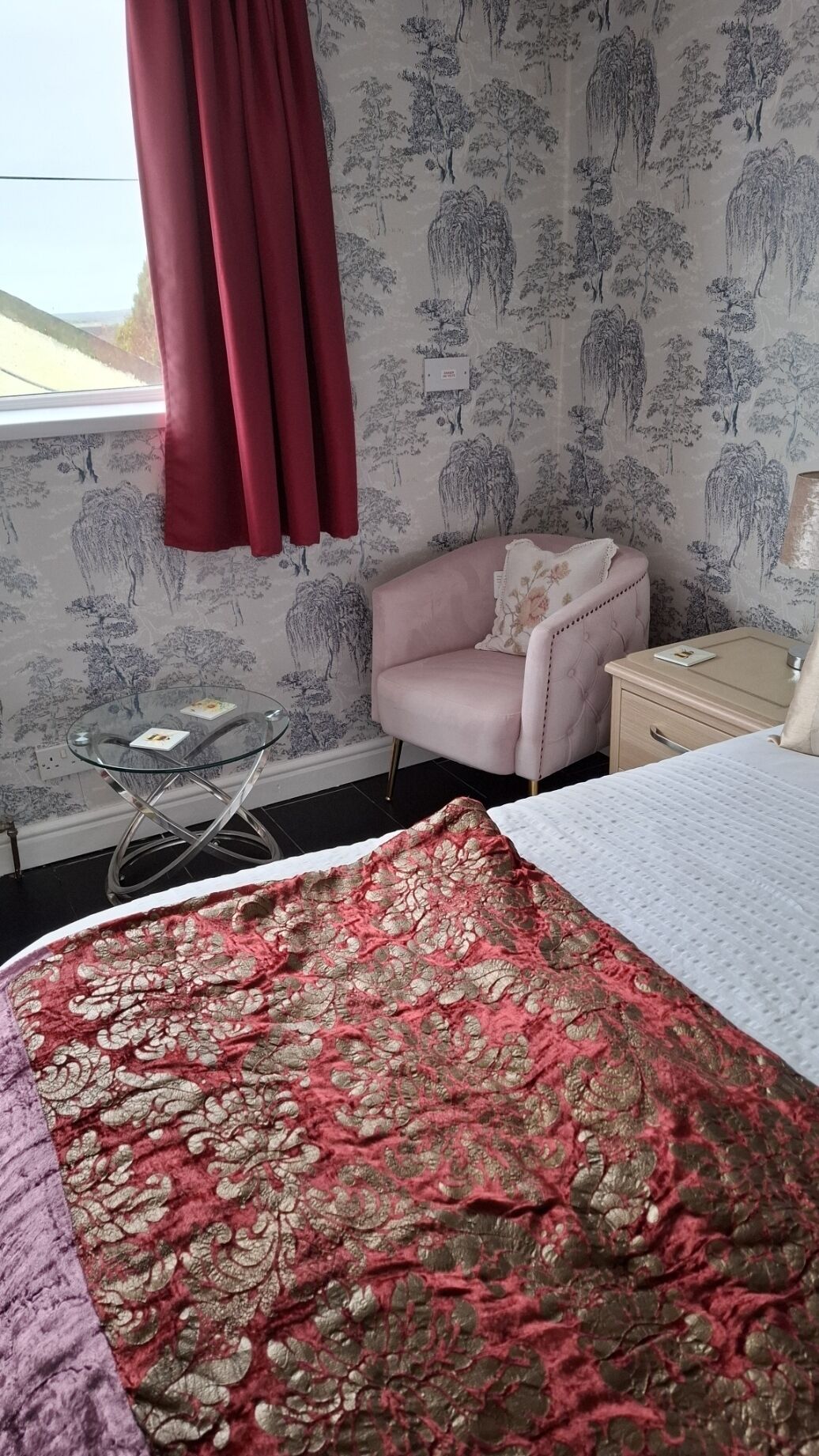 A bedroom with a bed, a pink armchair, a small glass table, and a nightstand.