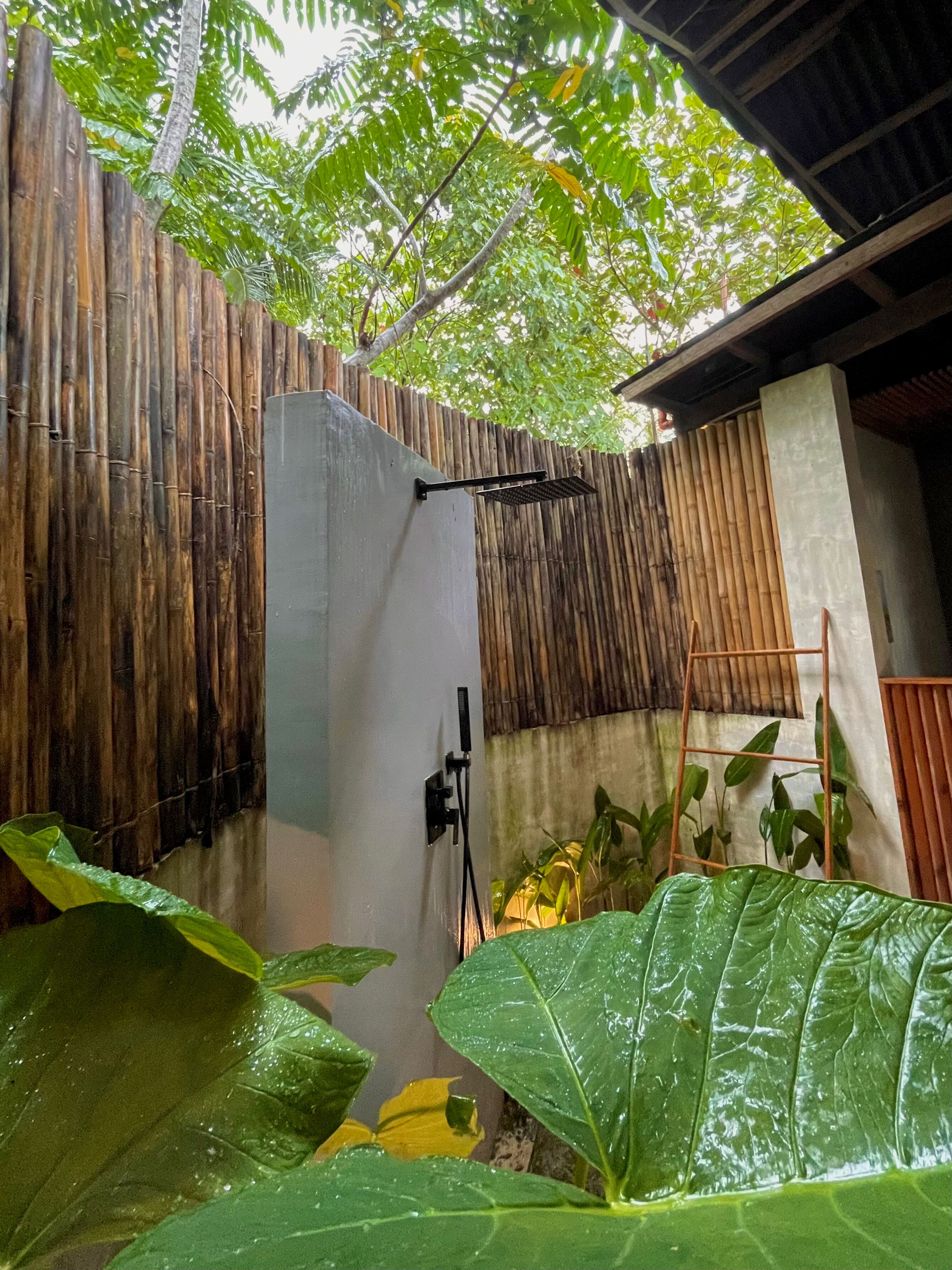 Un espacio al aire libre cubierto con una valla de bambú, un muro de concreto y una escalera metálica.