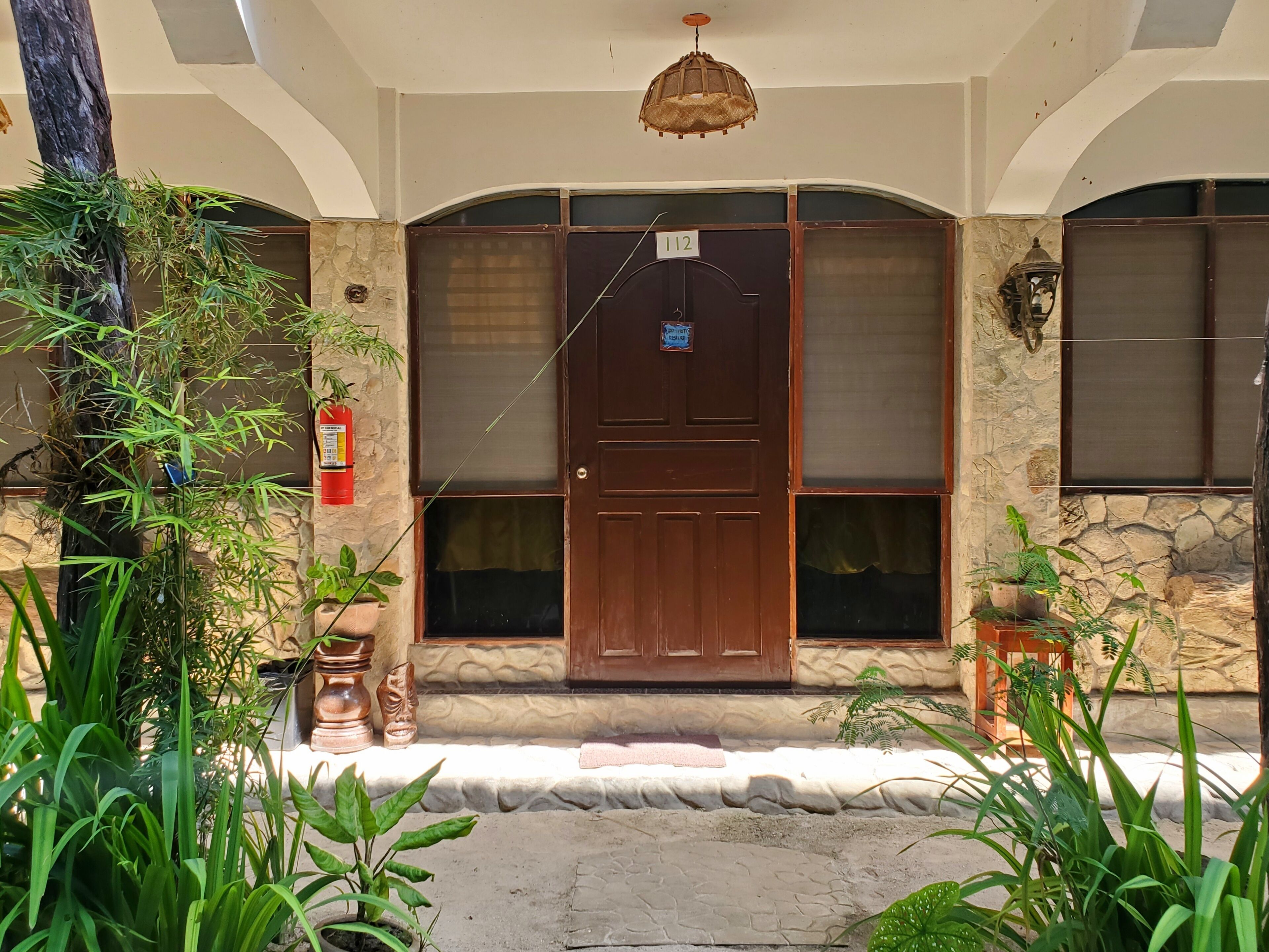 A building entrance with a wooden door, stone walls, and potted plants.