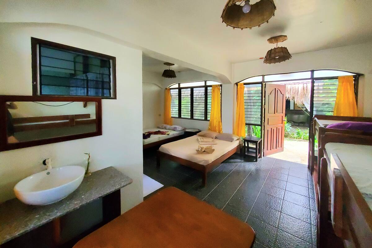 A room with a bed, a small table, a sink, and a window with curtains.