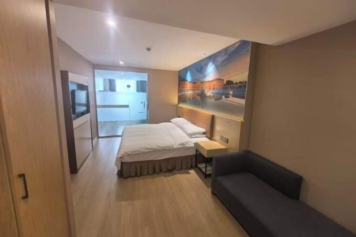 A hotel room with a bed, a sofa, a painting, and a television.
