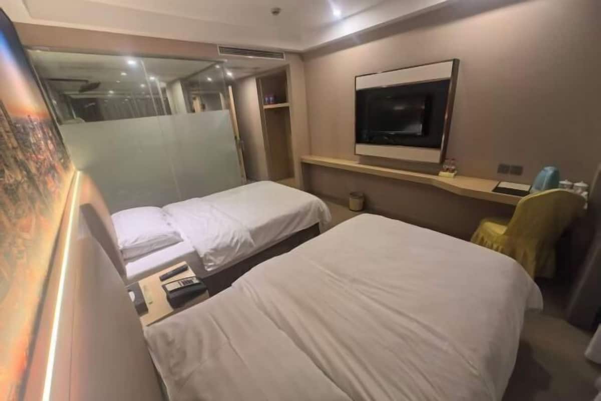A hotel room with two beds, a TV, a small shelf, and a painting on the wall.