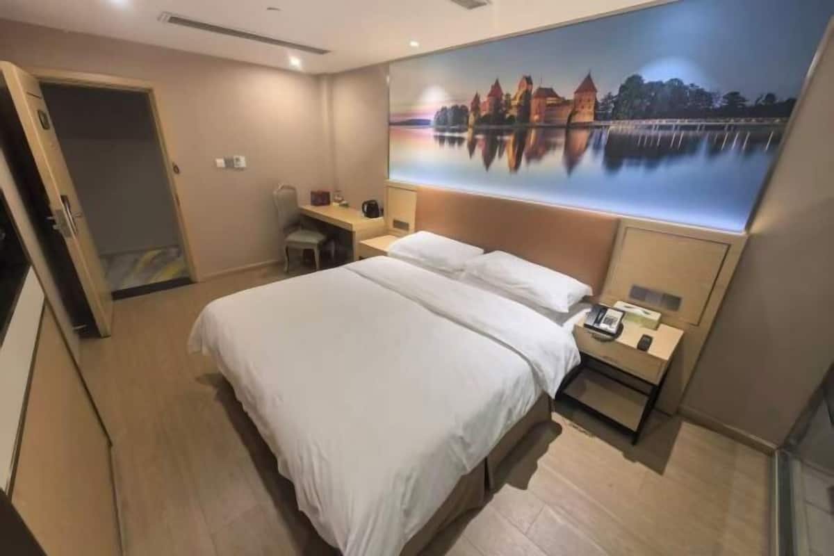 A hotel room with a bed, a desk, a chair, a nightstand, and a painting of a castle on the wall.