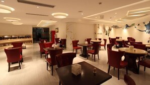 A modern restaurant interior with red chairs and tables, recessed ceiling lighting, and a marble wall with abstract art. - Vienna International Hotel (Shanghai Daning International Hongkou Guangyue Road Store) (Shanghai)