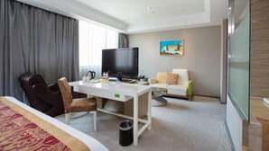 A hotel room with a bed, a desk with a flat-screen TV, a chair, a sofa, and a painting on the wall. - Vienna International Hotel (Shanghai Daning International Hongkou Guangyue Road Store) (Shanghai)