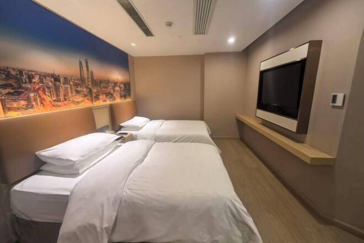 A hotel room with two beds, a large TV, and a cityscape mural on the wall.