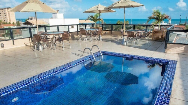 A rooftop pool area with blue-tiled pool, outdoor seating, and umbrellas. - Carmel Express Hotel (FORTALEZA)