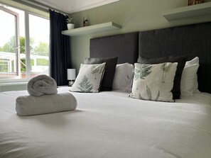 A neatly made bed with white linens, a rolled towel, and decorative pillows with a fern pattern. - Newlyn (Chester)