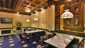 Un salón de conferencias con mesas dispuestas para una reunión, una pantalla de televisión y un techo decorativo.