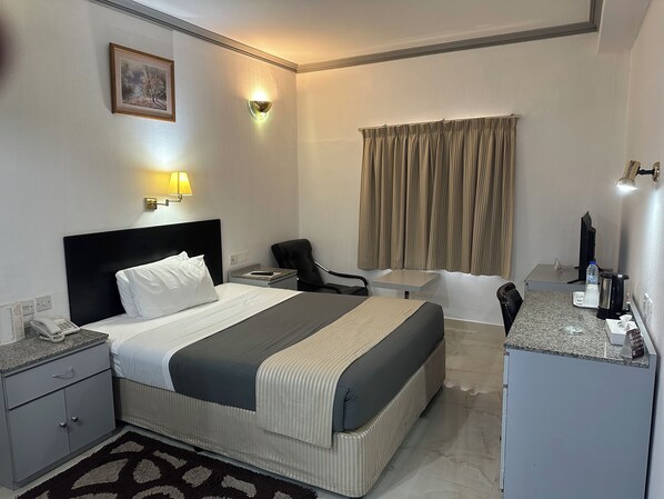 Habitación de hotel con cama, mesita de noche, silla, escritorio y una pequeña área de kitchenette.