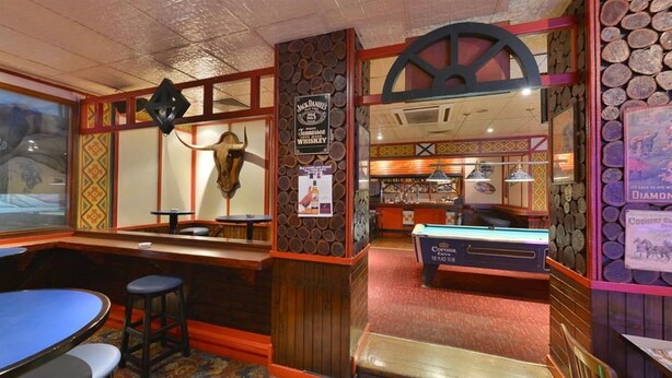 Zona de bar con taburetes, una mesa de billar y un letrero de whiskey.