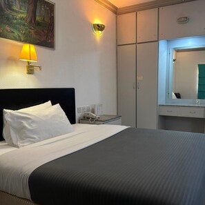 A hotel room with a bed, a bedside telephone, a wall-mounted lamp, a mirror, and a cabinet.