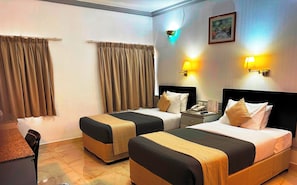 Habitación de hotel con dos camas, un escritorio y una silla. Hay cortinas, apliques de pared y un cuadro en la pared.
