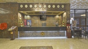 Un mostrador de recepción de hotel con un reloj, un cartel que dice 'Astoria Hotel' y un suelo de mármol.
