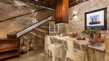 Une cuisine rustique avec un mur en pierre, un escalier en bois et un coin bar avec des chaises blanches.
