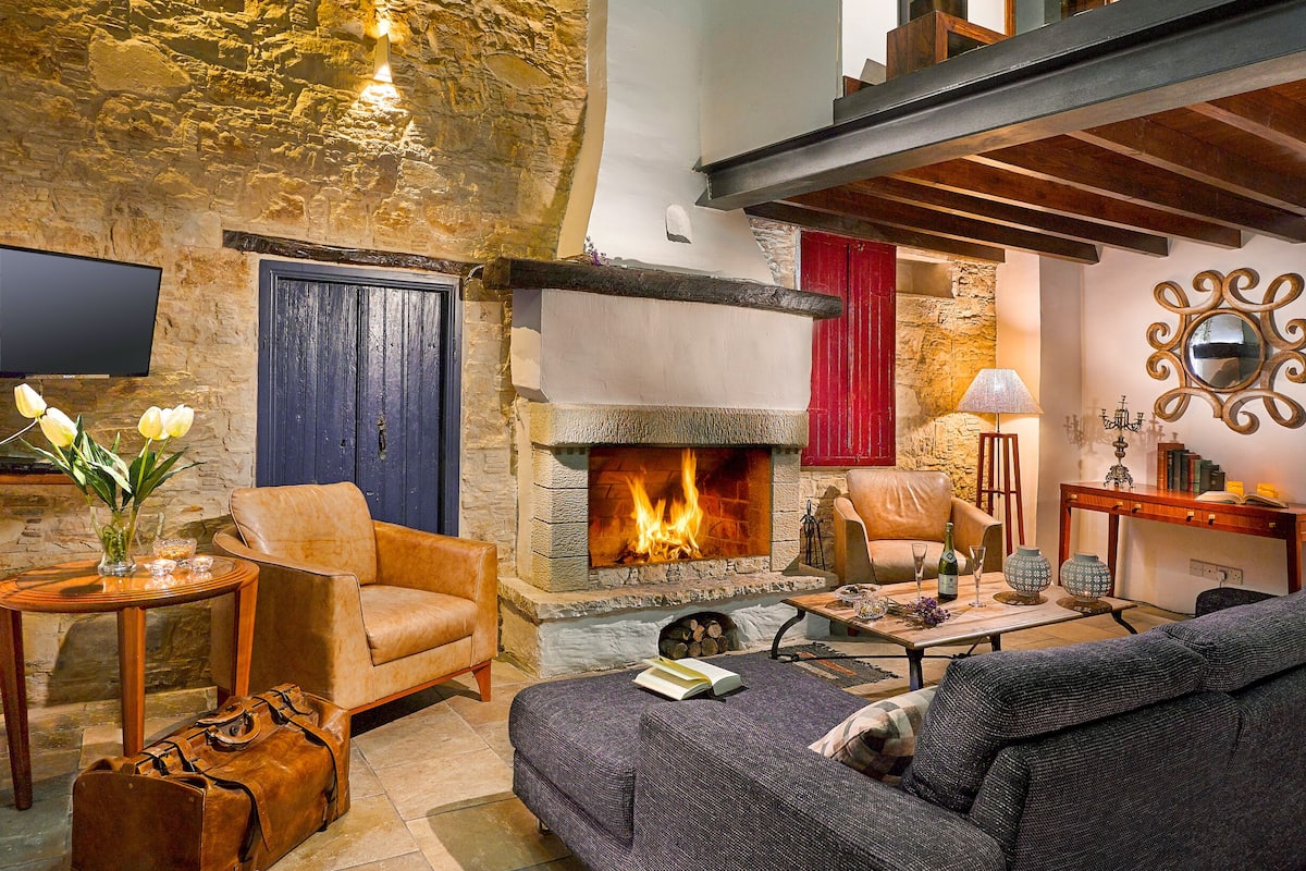 A cozy living room with a stone fireplace, leather furniture, and a flat-screen TV.