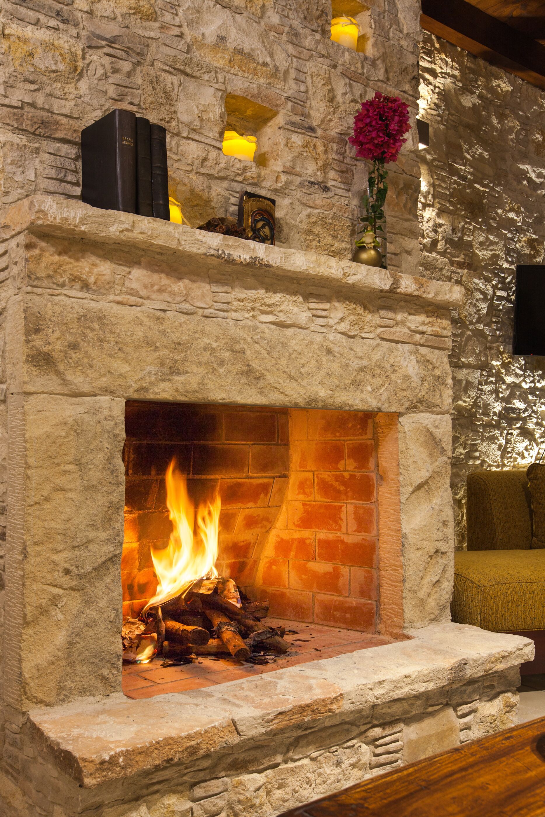 A stone fireplace with a fire, books, and a vase on a shelf above it.