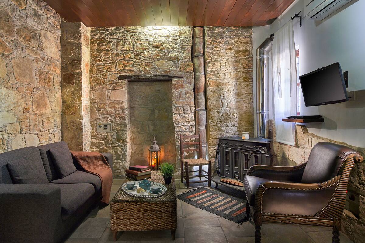 A cozy room with stone walls, a fireplace, a sofa, a chair, and a flat-screen TV mounted on the wall.