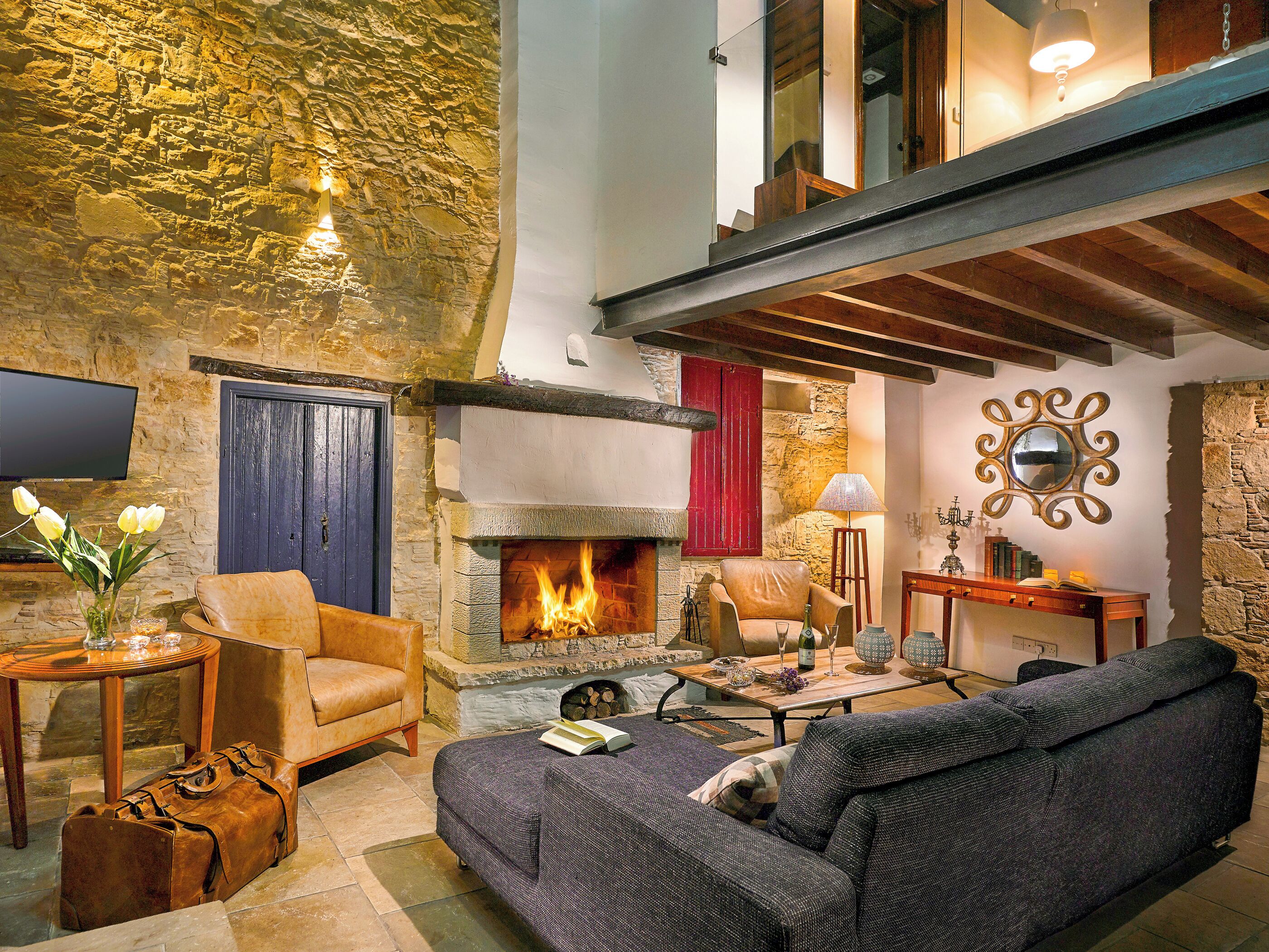 Ein gemütliches Wohnzimmer mit Steinwand, Kamin, Ledersessel, Sofa und Flachbildfernseher.