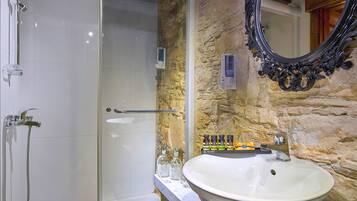 A bathroom with a glass shower enclosure, a white sink, and a stone wall.