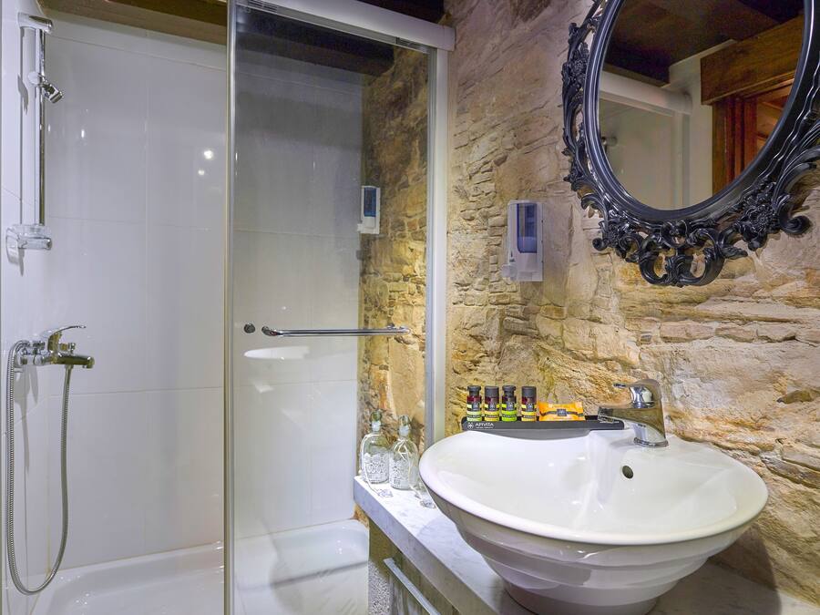 A bathroom with a glass shower enclosure, a white sink, and a stone wall.