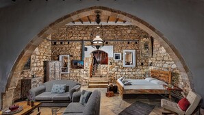 A rustic room with stone walls, a wooden ceiling, a sofa, a bed, and a staircase leading to an upper level.