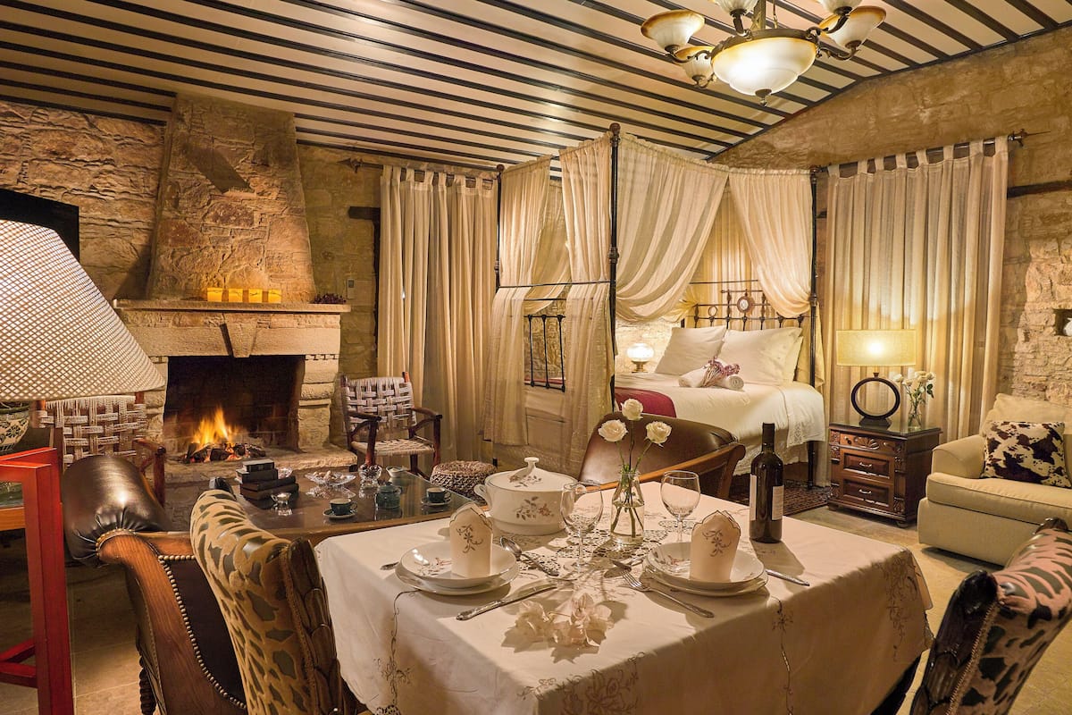 A cozy room with a fireplace, a bed with curtains, a dining table set for two, and a sofa.