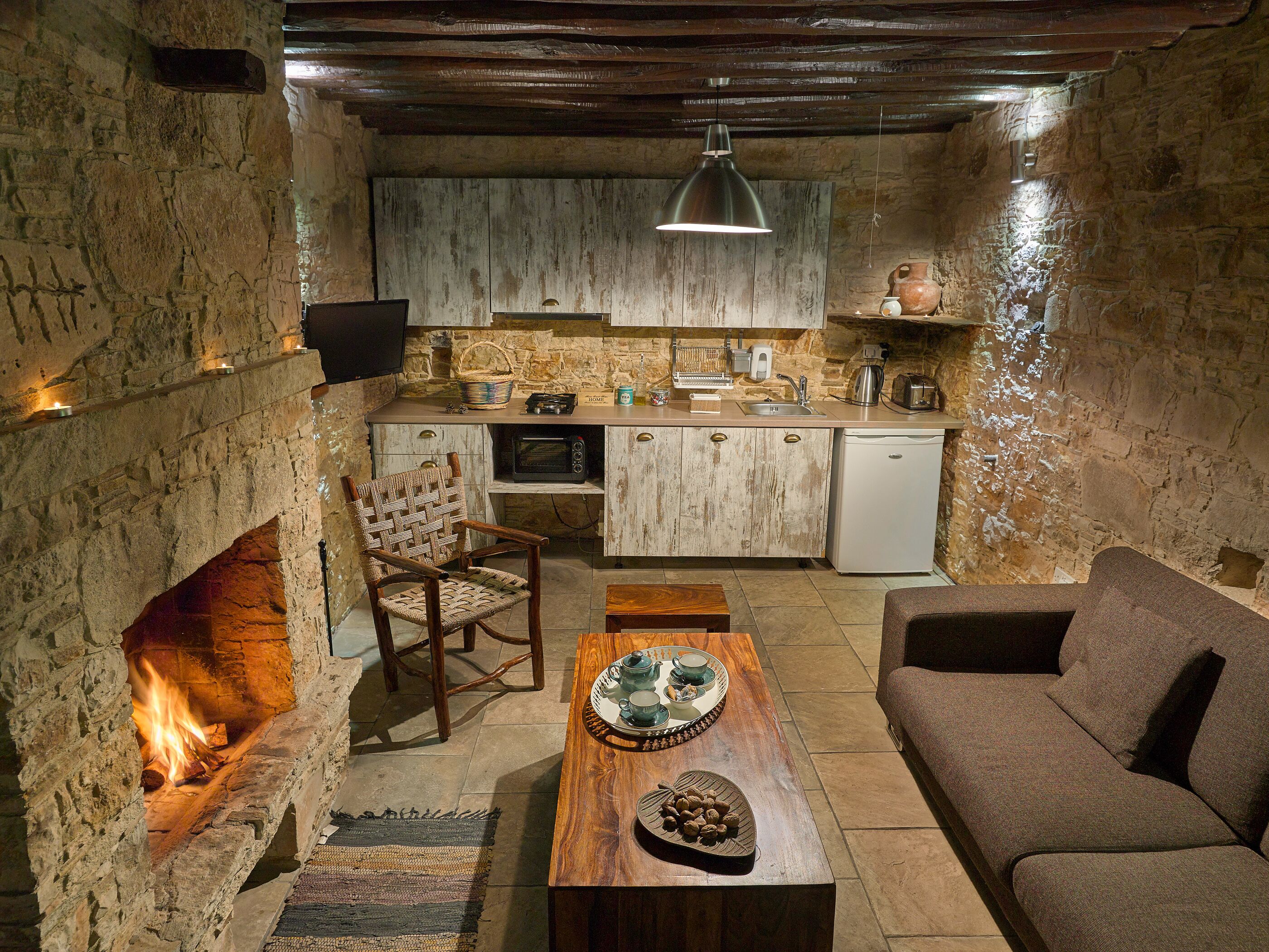 Un intérieur rustique avec une cheminée en pierre, des meubles en bois, un coin cuisine et un espace salon confortable.