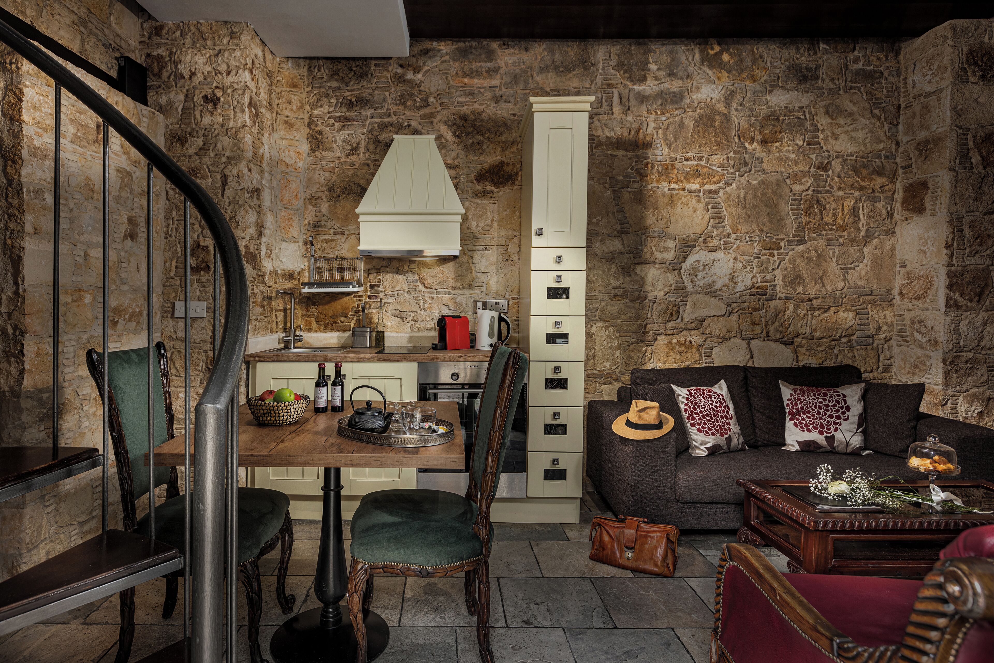 A rustic interior with a stone wall, a wooden dining table, chairs, a sofa, and a staircase.